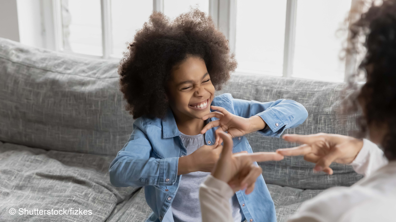 African deaf kid girl and her mother sitting on couch showing symbols with hands using visual-manual gestures enjoy communication at home. Hearing loss disability sign language learning school concept